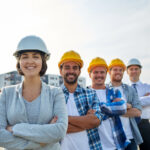 business, building, teamwork and people concept - group of smiling builders and architect in hardhats at construction site